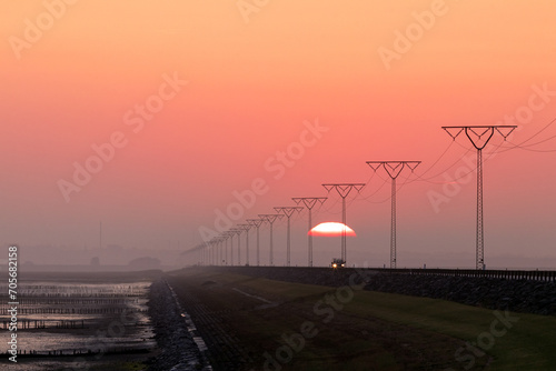 Scenic view to the Rømø causeway with 
transmission lines, fascines and red sky at sunrise. photo