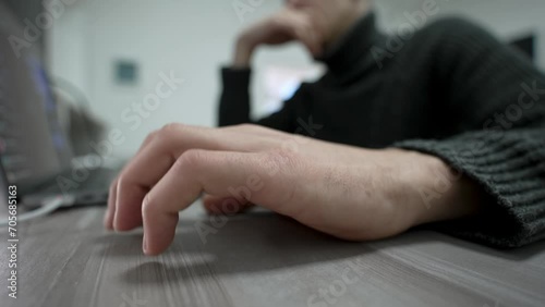 Bored man taps his fingers on table while sitting at his workplace near laptop. Close-up of man hand nervously tapping his fingers on table. Wide angle view male hand with gesture beat to music. photo