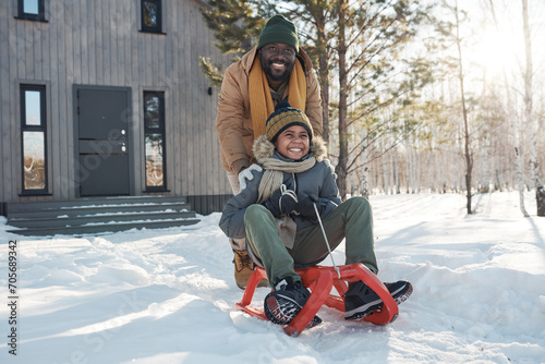 Photography Happy young African American man in warm winterwear pushing sledge with his son