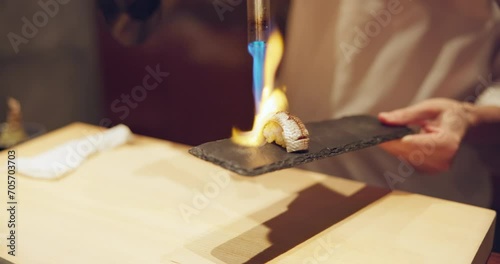 Hands, sushi and fire at restaurant for cooking, meal prep or food on table at diner, cuisine in night. Person, kitchen and blue flame with blowtorch, ready and service for nutrition, diet or snack photo