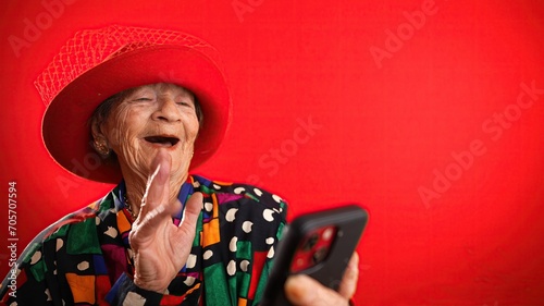 Funny fisheye view of old woman with no teeth having video chat on phone with family and friends isolated on red background.