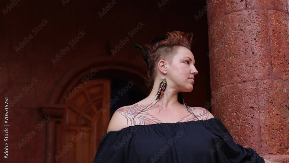 Charming woman with tattoos on her body, original feather decorations smiles in ancient building. 