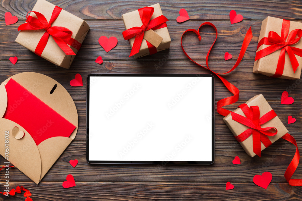 Fototapeta premium Top view of digital tablet with gift boxes and hearts on colorful background. Tablet with black screen with Holiday decorations gift box top view