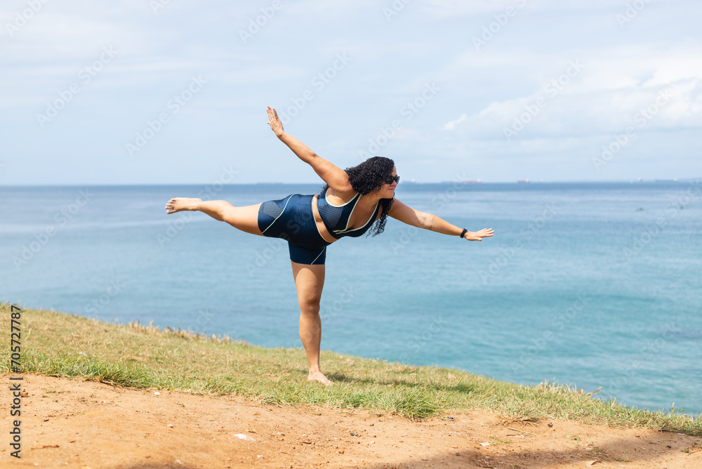 Beautiful, curly-haired woman standing on a hill, doing balance exercises. Beautiful, curly-haired woman standing on a hill, doing balance exercises.