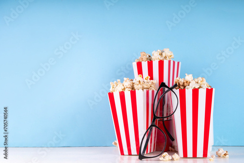 Cinema, film and movie night watching concept. Clapperboard, striped popcorn bucket boxes, with glasses on light blue background, copy space © ricka_kinamoto