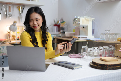 A young Asian woman, a small coffee shop entrepreneur, is using her mobile phone to send messages and talk with customers.