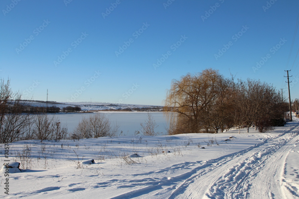 A snowy landscape with trees and a body of water in the distance