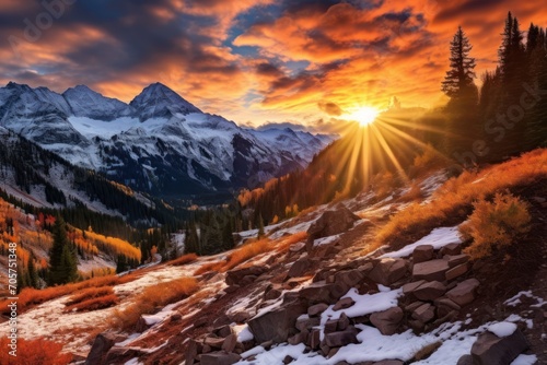  the sun is setting over a mountain range with snow on the ground and rocks in the foreground, and trees on the far side of the mountain, in the foreground.