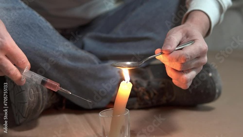 A drug addict cooks heroin on a spoon with the help of a candle fire. Drug addiction and homelessness concept.