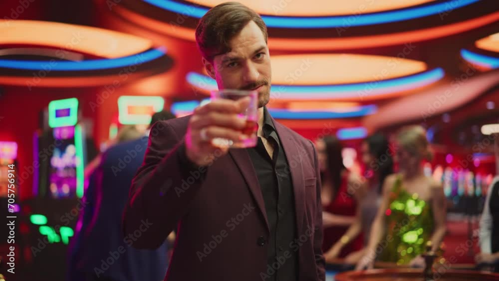 Portrait of a Sophisticated Young Man in an Expensive Suit, Smiling, Looking at Camera and Raising a Whisky Glass in a Luxurious Casino with Gamblers Playing Roulette in Colorful Bokeh Background Portrait of a Sophisticated Young Man in an Expensive Suit, Smiling, Looking at Camera and Raising a Whisky Glass in a Luxurious Casino with Gamblers Playing Roulette in Colorful Bokeh Background