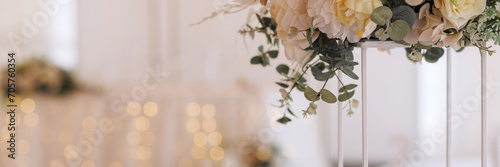Foto A bouquet of white and light yellow roses in a tall white vase with a gold base on a blurred background of a banquet hall