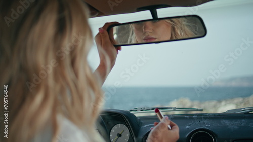 Girl adjusting car mirror sitting inside automobile holding red lipstick closeup
