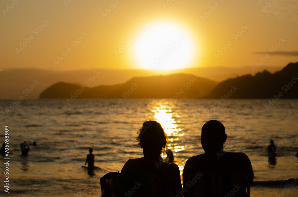 Amor à beira-mar: A silhueta do casal se funde ao pôr do sol, testemunhando a beleza do horizonte juntos.