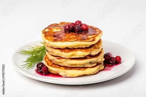  a stack of pancakes with cranberries and syrup on a white plate with a sprig of parsley on top of the plate, on a white background.