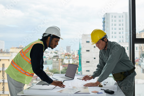 Engineer and construction worker bending over table with blueprints