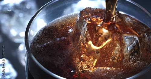 Super slow motion macro of fresh cool sparkling non alcoholic drink is being poured in transparent glass with ice cubes by bartender in bar or club. photo