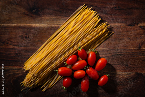 view of spaghetti pasta and datterini tomatoes on wooden table. typical ingredients of Italian cuisine