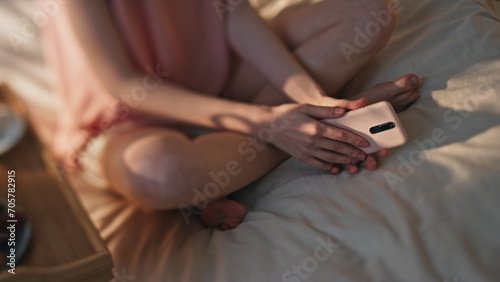 Female hands holding smartphone in sunny bed closeup. Hotel room breakfast table