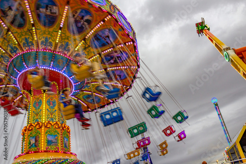 Detalhe de um brinquedo de rotação, grande e colorido, no parque de diversões com poucas pessoas, em um dia nublado.