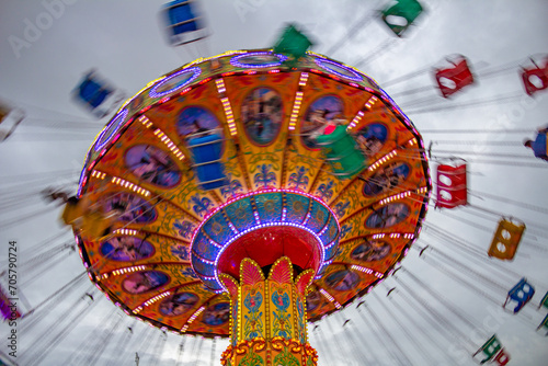 Um brinquedo de rotação, grande e colorido, no parque de diversões com poucas pessoas, em um dia nublado. Foto feita de baixo para cima.