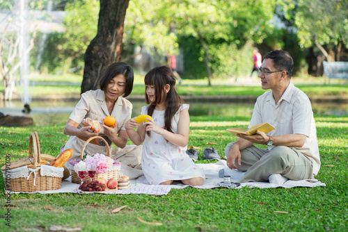 Happy family having picnic in the park with parents and kids sitting on the grass and enjoying healthy meals outdoors on a sunny summer day.