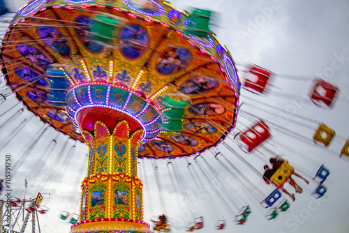 Um brinquedo gigante de rotação no parque de diversões com 2 pessoas em um dos balanços, em um dia nublado. Foto feita de baixo para cima. Imagem feita com baixa velocidade da câmera.