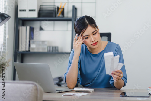 Worried asian woman managing finances on laptop at home office. photo