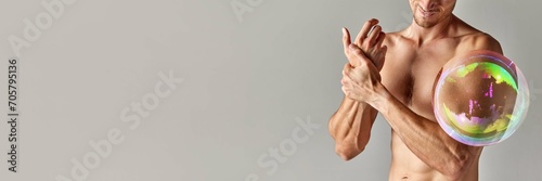 Cropped image of muscular shirtless male body, strong relief hands with soap bubble maximizing body part against grey background. Concept of male beauty, weight loss, diet, health. Banner