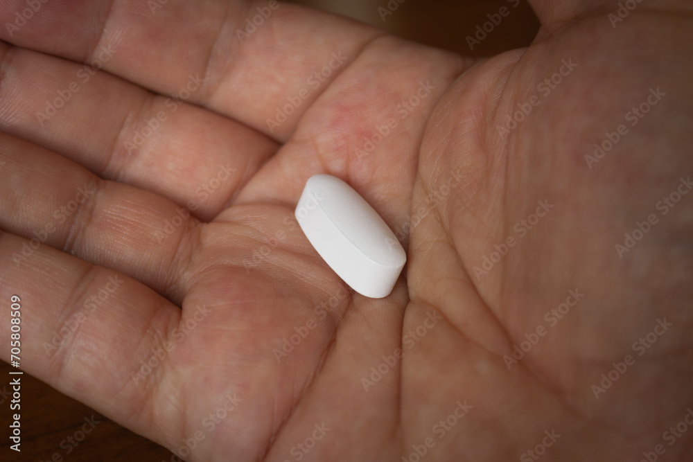Close-up of an adult hand holding a single white pill, healthcare concept Close-up of an adult hand holding a single white pill, healthcare concept