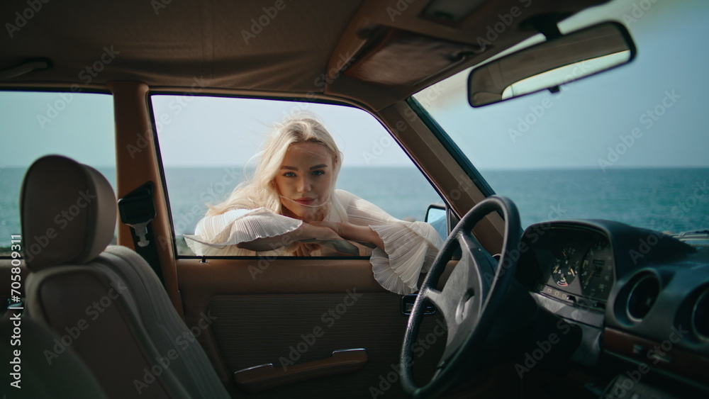 Woman leaning car door looking camera at seashore. Girl looking through window.