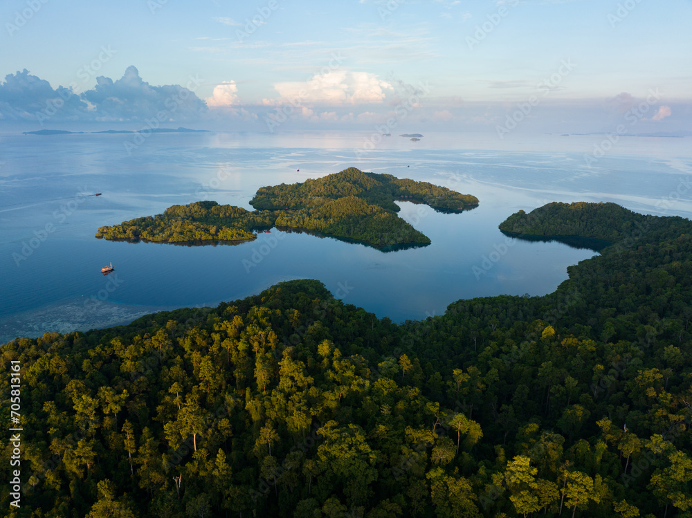 Sunrise illuminates calm seas around the islands of Gam and Yangeffo in Raja Ampat, Indonesia. This tropical region is mostly known for its exquisite coral reefs and overall high marine biodiversity.