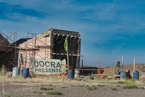 The image depicts a construction site with an unfinished brick building, scaffolding, and various construction materials scattered around. The main focus is an unfinished brick building with wooden © LSDemi
