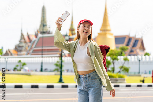 Young asian woman traveler with phone capturing moments and exploring Wat Phra Kaew and The Grand Palace in a happy and casual style during a sunny day © asean studio