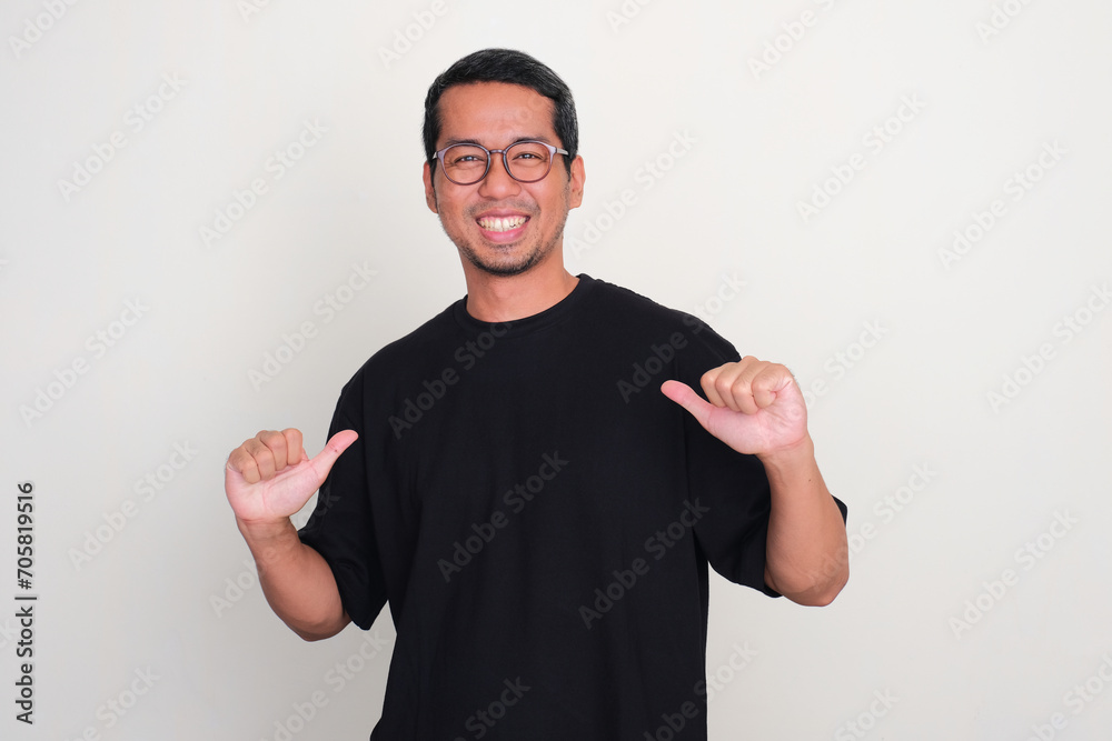 Fototapeta premium Adult Asian man pointing to plain black t-shirt that he wearing with happy expression