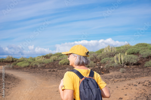 Back view of carefree senior woman in yellow walking in outdoor footpath in a sunny day. Weekend tourism and people leisure outdoor activity concept lifestyle.