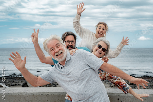 Playful multi generation family having fun together on outdoor excursion at the seaside, gesturing towards the camera. Parents, son and daughter-in-law enjoying free time and recreational activities