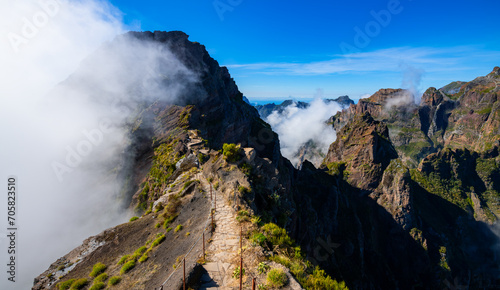 “Ninho da Manta“ a panoramic walk near “Pico do Arieiro“ peak, Madeira island Portugal. Narrow mountain ridge with steep precipice both sides the trail. Scenic panorama with clouds and blue sky.