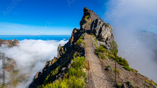 “Ninho da Manta“ a panoramic walk  near “Pico do Arieiro“ peak, Madeira island Portugal. Iconic mountain trail with steep precipice both sides the path. Scenic panorama with mist and blue sky.