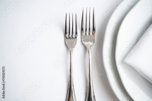 Place setting. Clean  minimal  white plates  white tablecloth  stainless forks  shallow depth of field. 
