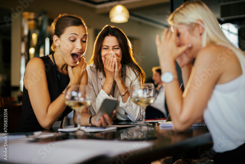 Women friends excitedly looking at smartphone in restaurant photo