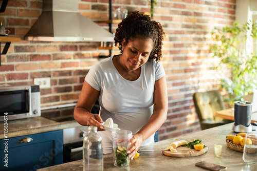 Young pregnant woman making a healthy smoothie in the kitchen photo