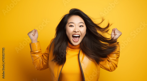 Femme asiatique jeune, heureuse, souriante, bras levés, poings serrés, arrière-plan orange