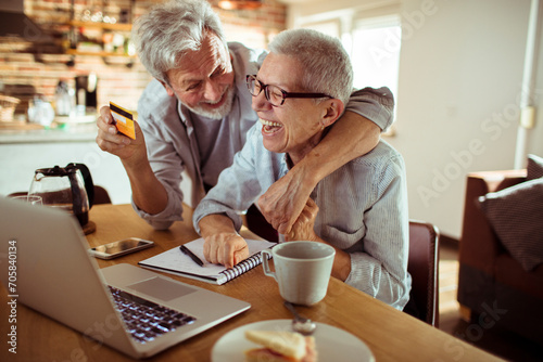 Happy senior couple using credit card on laptop at home