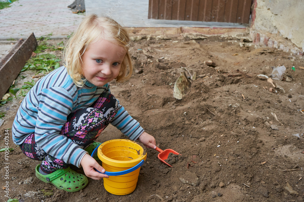 little girl is playing on the construction site, a child is playing in the yard with a bucket and a shovel little girl is playing on the construction site, a child is playing in the yard with a bucket and a shovel