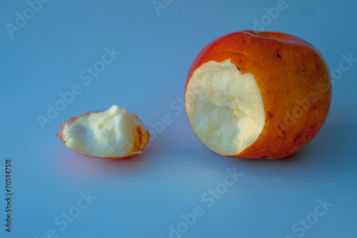 Fairy tale concept with a poisoned bitten red apple. Inedible apple peel. Blue background.