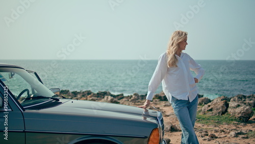 Stylish model posing retro car at summer seacoast. Woman standing sunny beach.