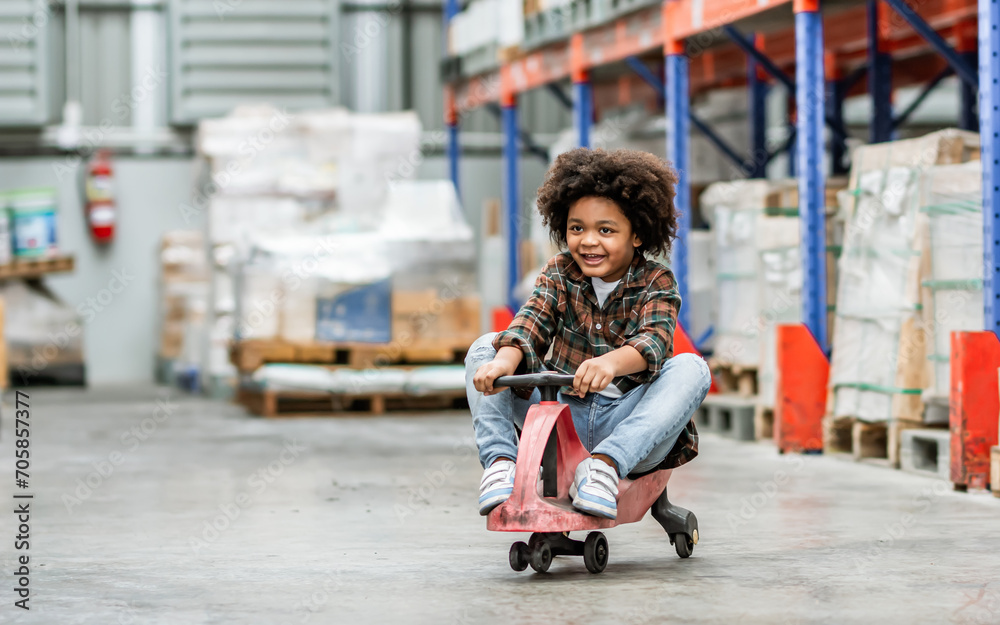 Little african afro hair boy wearing casual shirt, playing with happiness in warehouse or factory in holiday, riding bike or scooter, funny smiling. Kid, Education, Leisure Concept.