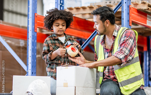 Canvas Print Little boy wearing safety hard hat deliver box or parcel to worker in factory for shipping to customer, smiling with happiness