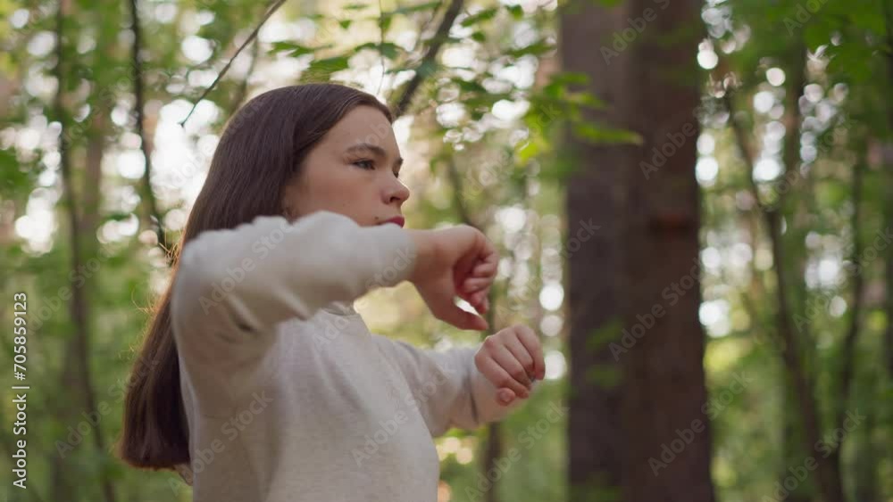 Woman warms up before cardio workout in forest. Lady does arms turning exercise preparing for long run surrounded by dense trees at sunlight. Training in nature at sunset Woman warms up before cardio workout in forest. Lady does arms turning exercise preparing for long run surrounded by dense trees at sunlight. Training in nature at sunset