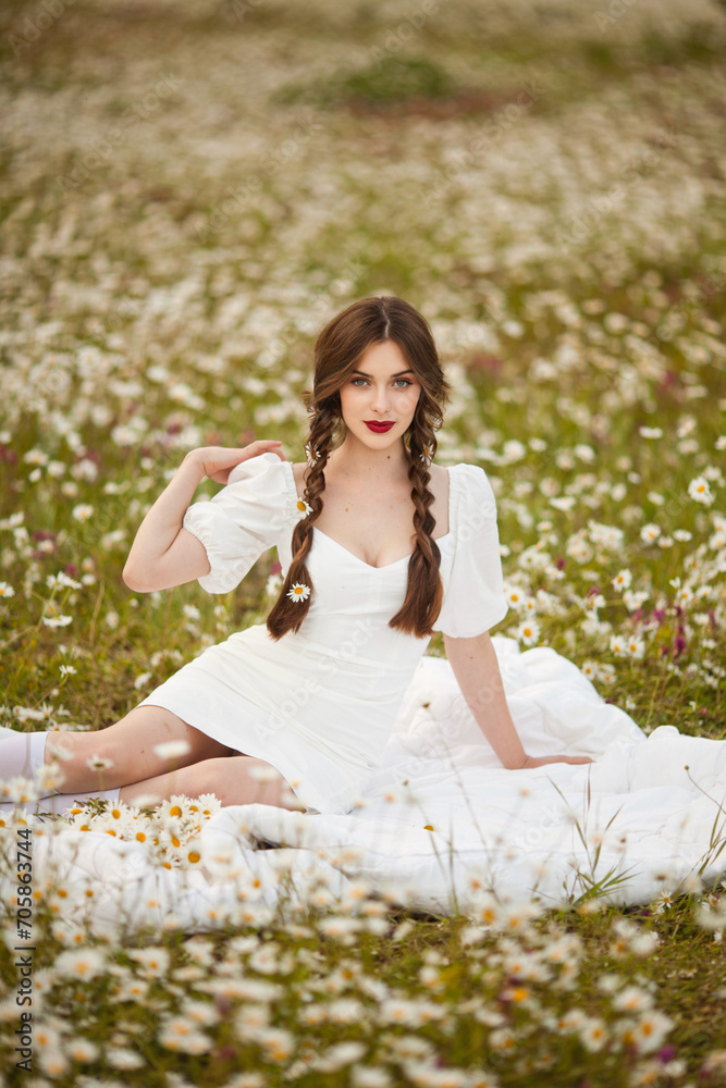 close portrait of a beautiful, laughing woman in a light dress holding a chamomile near her face during sunset, lit from the back
